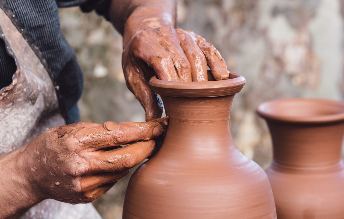 Close up view of an adult male using their own hands to make a ceramic vase.